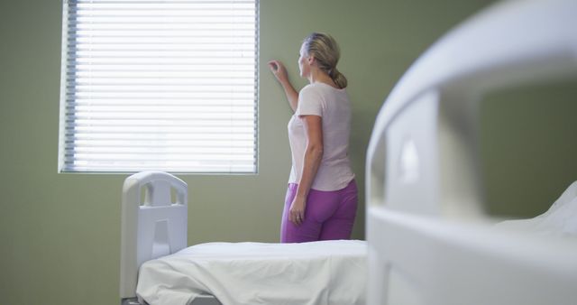 Caucasian female patient standing in hospital room looking at window. medicine, health and healthcare services.