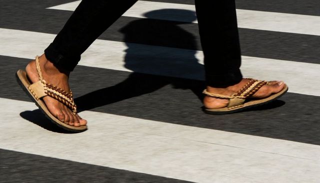 Braided sandals crossing zebra crosswalk casting shadow, urban walking motion