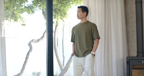 Asian man standing by glass window wearing watch and linen trousers in bright interior