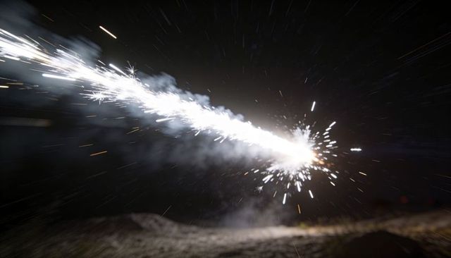 Shooting spark trail cutting across night sky with exploding white core, embers and smoke