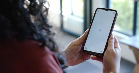 African american woman holding smartphone with blank screen near window for app mockup