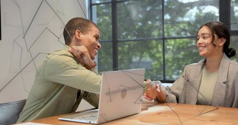 Business professionals shaking hands across modern office table with laptop and daylight