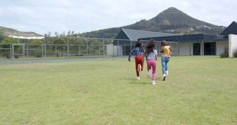 Girls Running on Grass Field Near School Building in Springtime