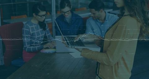 Standing woman presenting with laptop to team in office, data overlay, collaboration