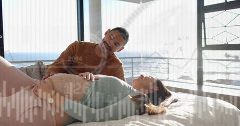 Expectant couple sharing tender moment in sunlit bedroom, partner touching belly