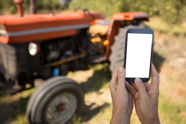 This image shows a woman holding a mobile phone with a blank screen in an olive farm, with a tractor in the background. It can be used for themes related to agriculture, technology in farming, rural lifestyle, and outdoor activities. Ideal for articles, blogs, and advertisements focusing on modern farming techniques, agricultural apps, and rural connectivity.