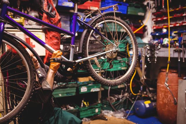 Mechanic repairing bicycle in workshop filled with tools and equipment. Ideal for use in articles about bicycle maintenance, professional repair services, cycling enthusiasts, and mechanical workshops. Can be used in promotional materials for bike repair shops, instructional guides on bike maintenance, and advertisements for mechanical tools and equipment.