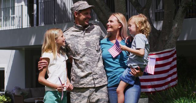 Father in military uniform rejoins family, wife and children hold American flags, strong sense of patriotism and happy reunion. Perfect for themes like military homecomings, family reunions, patriotism, US holidays, and support for troops.