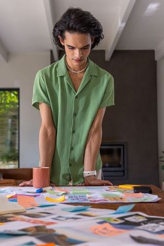 Creative professional leaning over workspace sorting printed visuals and sticky notes