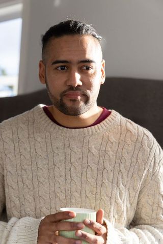 Sunlit asian man relaxing with mug in cozy cream cable knit sweater at home