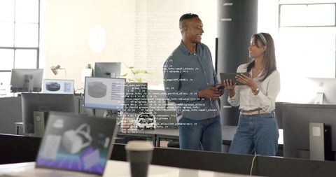 Developers collaborating with tablet and monitors in open office with code overlay