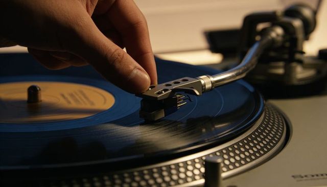 Hand guiding tonearm onto spinning vinyl record on turntable close-up