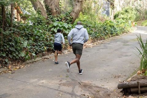 Father and son running uphill on tree-lined driveway wearing hoodies and running shoes