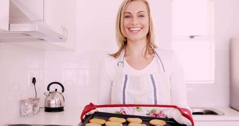 Smiling Woman Presenting Freshly Baked Cookies in Modern Kitchen - Download Free Stock Images Pikwizard.com