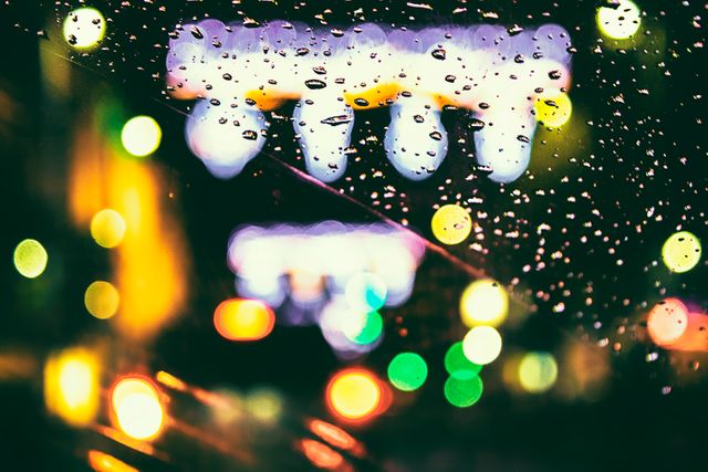 Raindrops on window with blurry city lights creating bokeh effect. Ideal for backgrounds, urban themes, rainy night concepts, and creative projects highlighting city life and colorful blur aesthetics.