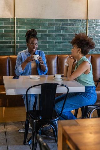 Two african american women chatting over coffee in cozy cafe booth casual conversation