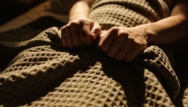 Clenched hands gripping waffle-weave blanket conveying anxiety and sleepless tension