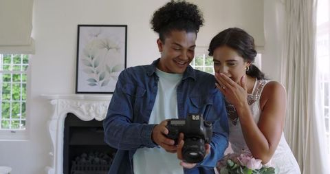 Excited photographer and bride reviewing photos on camera screen indoors