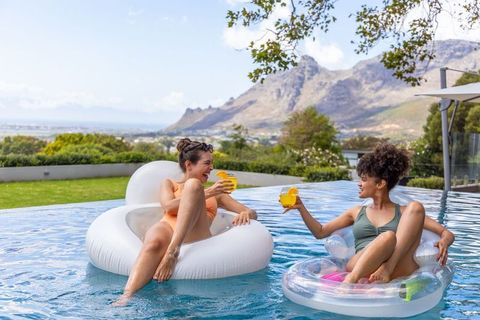Friends floating and toasting on inflatables in backyard pool with mountain view
