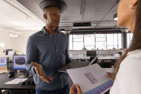 Diverse Team Reviewing Bar Chart on Laptop in Open-Plan Office Collaborating on Data