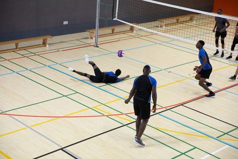 African american men's volleyball team diving and digging on indoor hardwood court