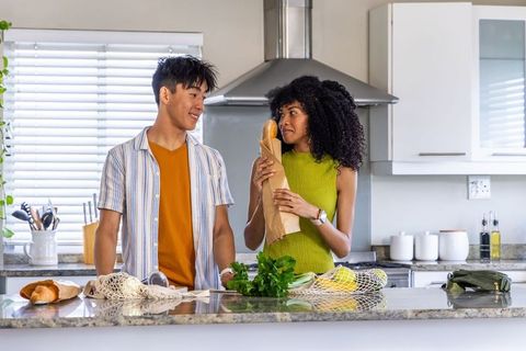 Multicultural couple preparing groceries on modern kitchen island with baguette and herbs