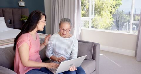 Mother and Daughter Using Laptop Together in Sunny Living Room