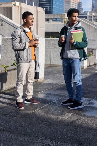 African american students standing on urban campus terrace holding coffee and notebooks