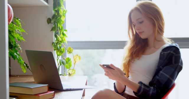 Young Woman Browsing Smartphone Next to Laptop at Desk - Download Free Stock Images Pikwizard.com