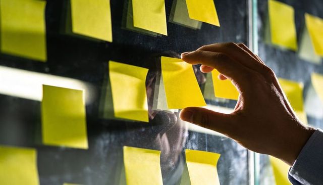 Hand placing yellow sticky notes on glass for agile planning and team brainstorming