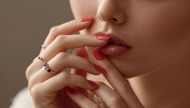Elegant Woman With Coral Nails and Gemstone Rings in Thoughtful Pose