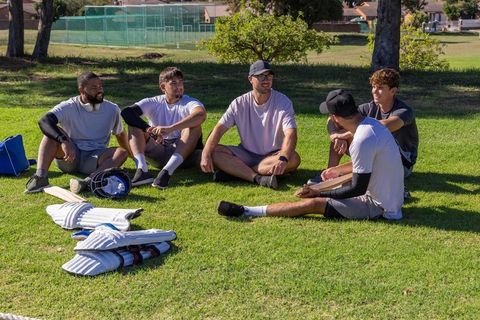 Multicultural cricket teammates chatting and relaxing on sports field after practice