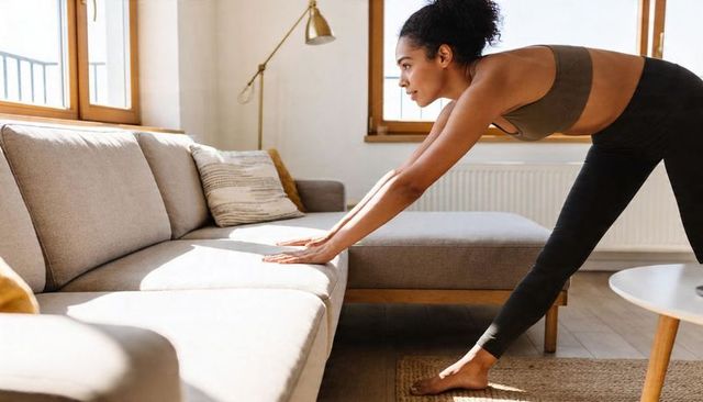 Woman stretching on sectional sofa in sunlit living room — morning home workout