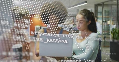 Collaborating women developers reviewing code on laptop with overlay in modern workspace