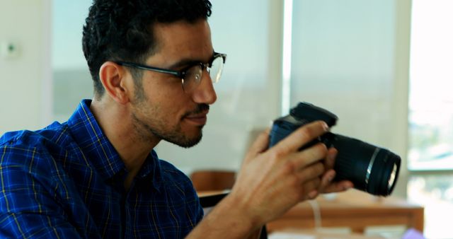 A young Middle Eastern man examines a camera closely, with copy space. His focus and the camera suggest he may be a photographer or a photography enthusiast.