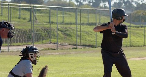 Right-handed batter preparing to swing facing catcher and umpire on sunlit baseball field