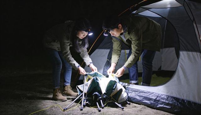 Couple assembling dome tent at night using headlamps and poles while camping outdoors