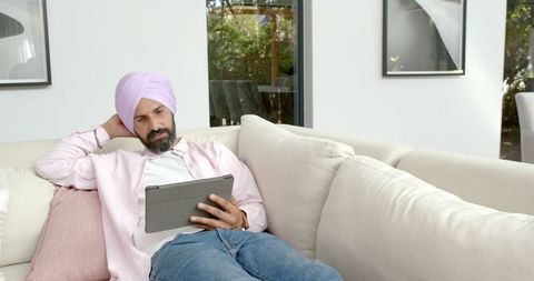 Man Relaxing on Couch Browsing Tablet at Home