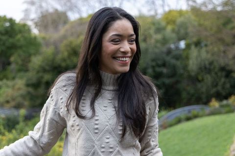 Smiling woman wearing beige cable-knit sweater standing in green garden with turtleneck