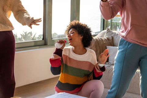 Diverse friends singing and dancing in cozy living room with portable bluetooth microphone speaker