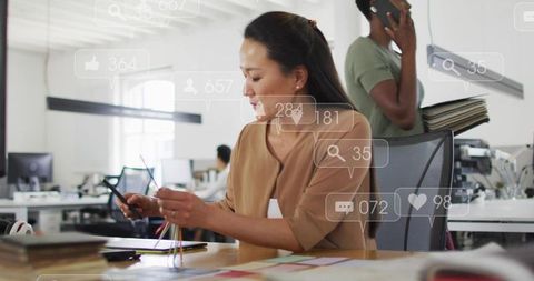 Korean designer working with color swatches at open-plan office with social overlays