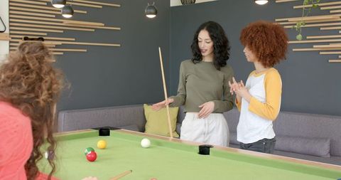 Diverse friends discussing pool shot in contemporary lounge playing casual billiards