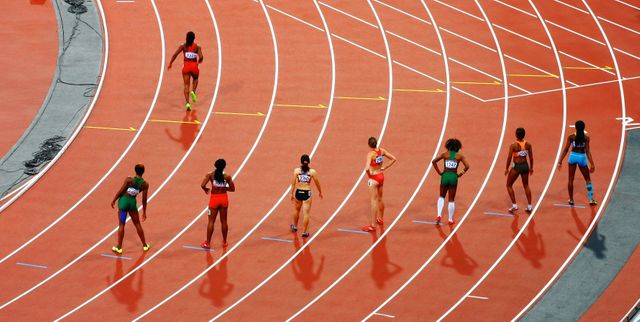 Athletes are competing in a sprint race on a track. Overhead view highlights the lanes and uniform starting positions. Perfect for illustrating themes related to sports, competitions, athletics, and fitness events. Ideal for use in sports-related blogs, fitness sites, competition coverage, and promotion of athletic events.