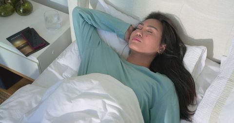 Mid adult asian woman sleeping peacefully in bed wearing teal top with bedside phone
