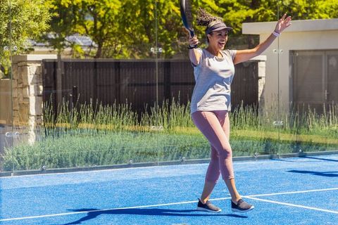 African american woman celebrating winning point on blue outdoor paddle court with glass walls