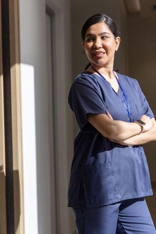 Confident nurse standing in sunlit corridor wearing navy scrubs and id lanyard