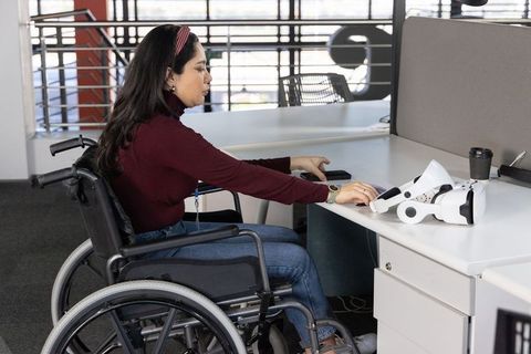 Woman in wheelchair reaching for smartphone and prosthetic at modern inclusive workspace