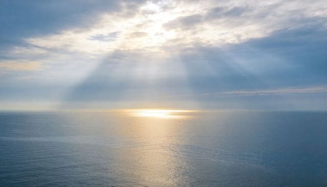 Sunbeams breaking through clouds reflecting golden patch on calm ocean horizon