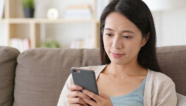 Calm woman using smartphone on sofa at home, scrolling content, remote work and digital life