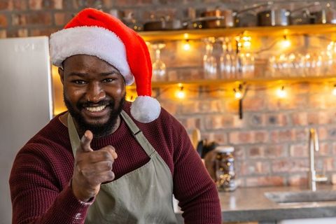 African american barista wearing santa hat smiling and pointing in cozy festive cafe kitchen
